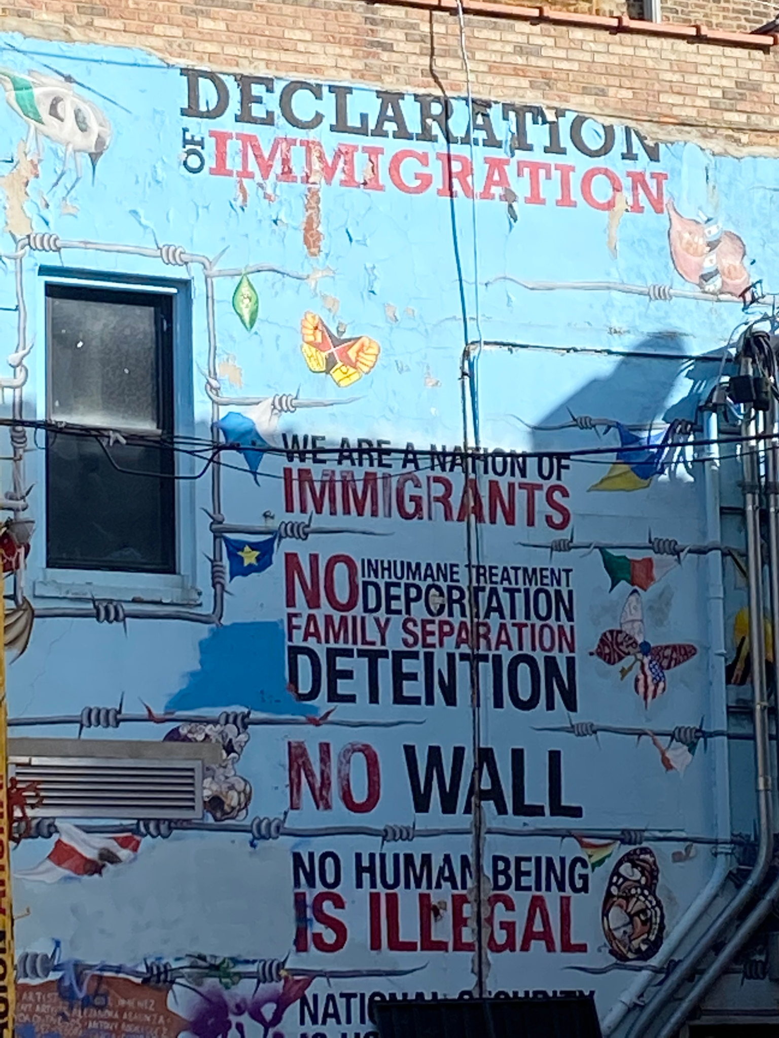 This mural is “Declaration of Immigration,” and depicts the text “Declaration of Immigration; We are a nation of immigrants; No inhumane treatment, deportation, family separation, detention; No wall; No human being is illegal.” Depicted in between these statements are barbed wire and a variety of national flags from Latin America. 